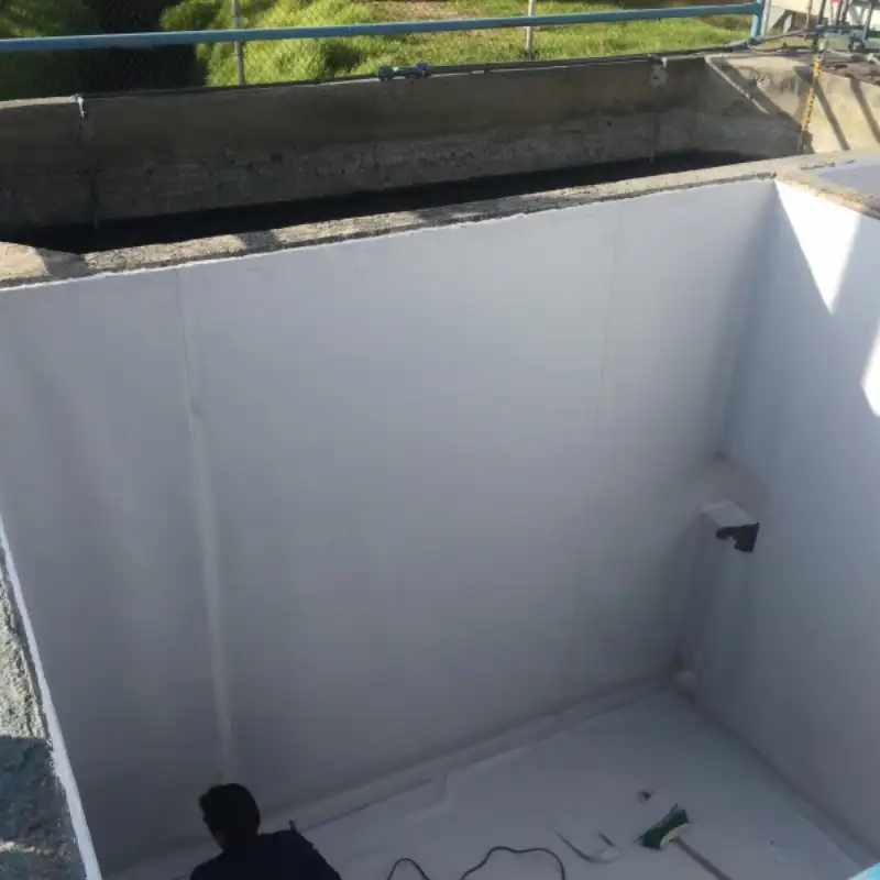 Interior de una cisterna o depósito de agua con las paredes recubiertas de un mortero cementoso blanco, anti-hidrostático. Un técnico en el fondo verifica la correcta aplicación del recubrimiento para asegurar el agua potable en casas residenciales.