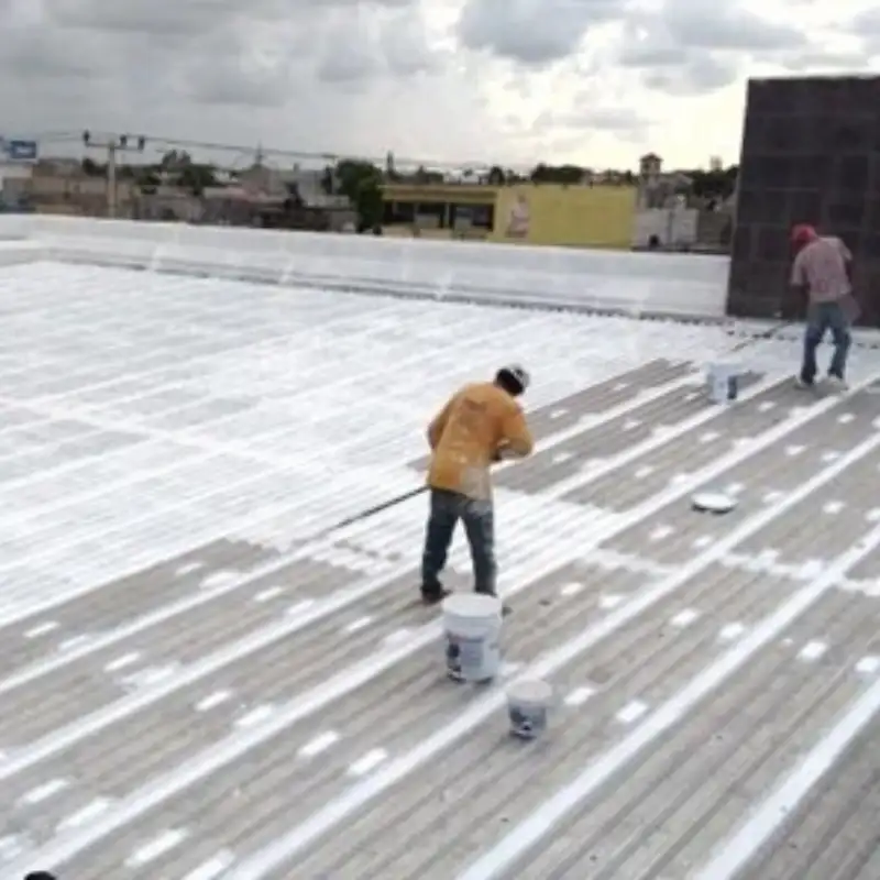 Dos técnicos de Quantumef aplicando un sistema impermeabilizante blanco con rodillo sobre una cubierta metálica estriada en una nave industrial en Iztapalapa. La solución proporciona resistencia química y elimina goteras, asegurando la maquinaria.