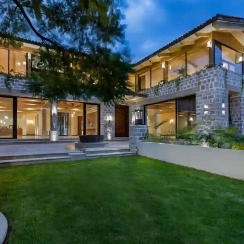 Imponente casa habitación de lujo con fachada de piedra y grandes ventanales, jardín frontal, ubicada en Jardines del Pedregal, ideal para proyectos llave en mano y mantenimiento residencial en CDMX.