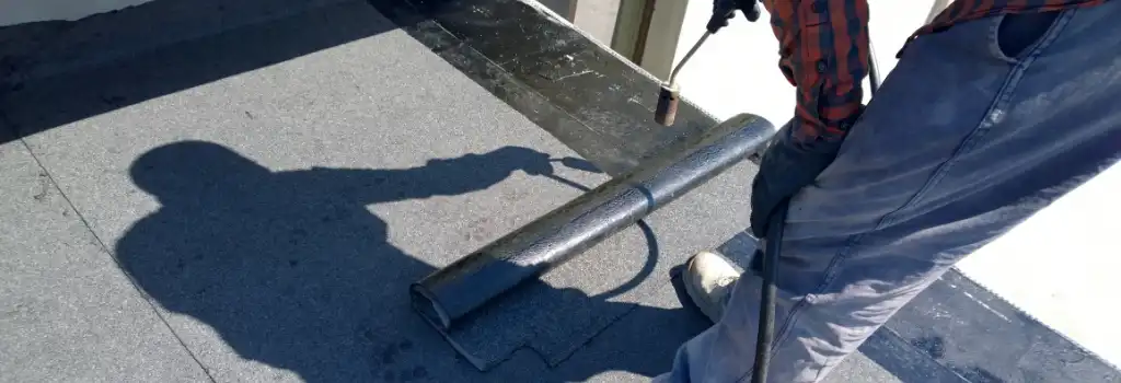 Obrero especializado utilizando un soplete para fusionar un rollo de manto prefabricado sobre una azotea gris. Este sistema de impermeabilización profesional de alto rendimiento detiene filtraciones y humedad, ideal para casas y edificios en municipios como Naucalpan o Tlalnepantla.