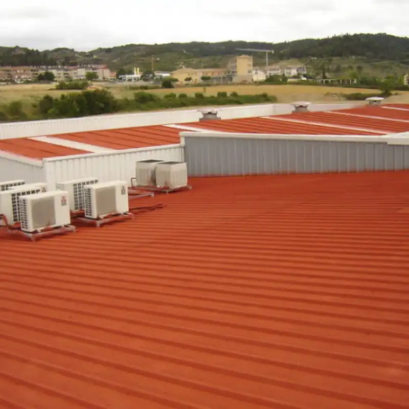 Vista aérea de la cubierta metálica de una nave industrial recién impermeabilizada con un recubrimiento rojo, equipada con unidades de aire acondicionado. Quantumef ofrece sistemas prefabricados y acrílicos para proteger techos y losas de edificios y casas en el Edomex.