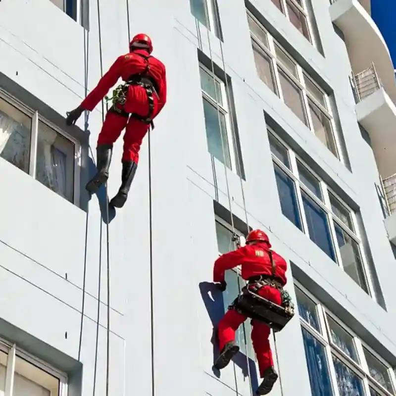 Dos técnicos de Quantumef S.A. de C.V. realizando trabajos de pintura en la fachada de un edificio corporativo con equipos de seguridad y arnés, destacando la experiencia en trabajos de altura y pintura e impermeabilización en Polanco.